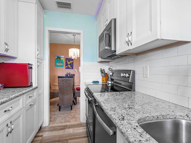 kitchen featuring pendant lighting, backsplash, light wood-type flooring, white cabinetry, and stainless steel appliances