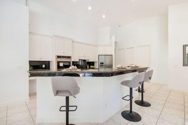 1627 Mayacoo Lakes Blvd, West Palm Beach, FL 33411 - kitchen featuring stainless steel appliances, high vaulted ceiling, a kitchen breakfast bar, dark countertops, and white cabinets