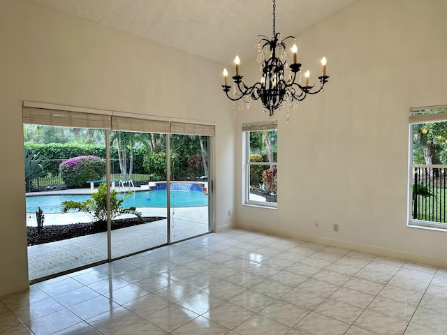 spare room with a wealth of natural light, light tile patterned floors, high vaulted ceiling, and an inviting chandelier