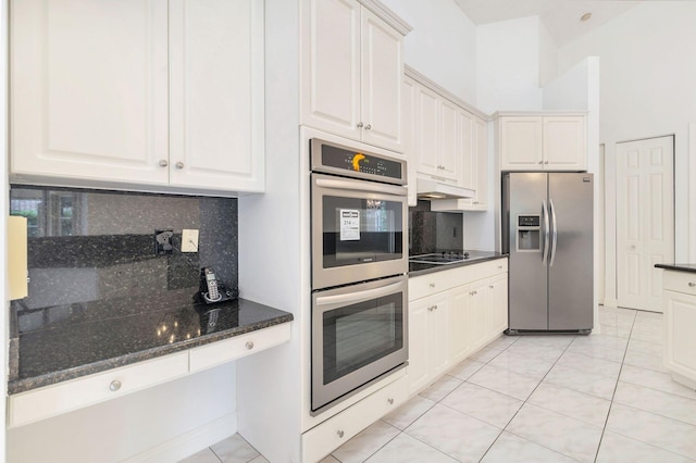 kitchen featuring white cabinetry, backsplash, dark stone counters, light tile patterned floors, and appliances with stainless steel finishes