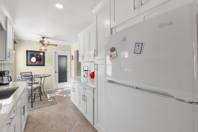 kitchen with light stone counters, ceiling fan, white refrigerator, white cabinetry, and light tile patterned flooring