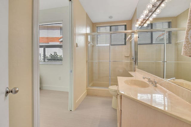 bathroom featuring vanity, toilet, a shower with door, and a wealth of natural light