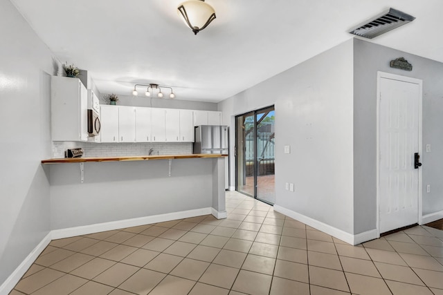 kitchen with white cabinetry, backsplash, kitchen peninsula, a kitchen bar, and appliances with stainless steel finishes