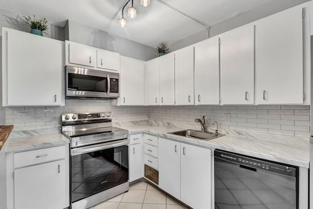 kitchen with appliances with stainless steel finishes, tasteful backsplash, sink, white cabinetry, and light tile patterned flooring