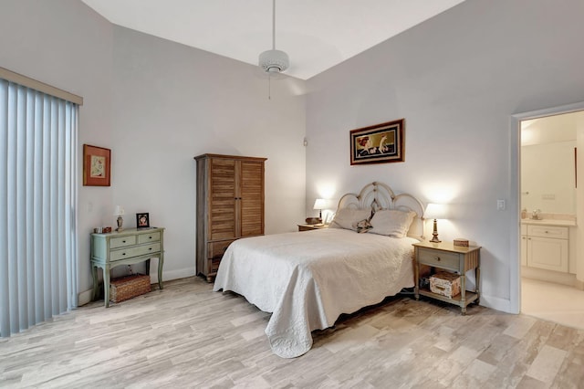 bedroom with ceiling fan, light hardwood / wood-style floors, a high ceiling, and ensuite bath