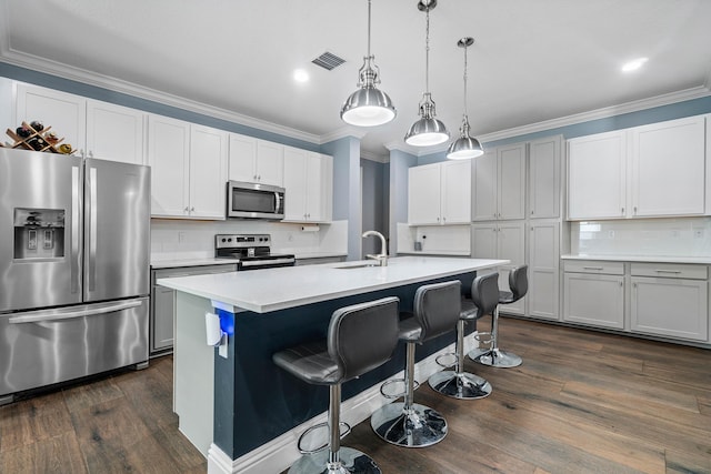 kitchen with dark wood-type flooring, an island with sink, appliances with stainless steel finishes, decorative light fixtures, and a kitchen bar