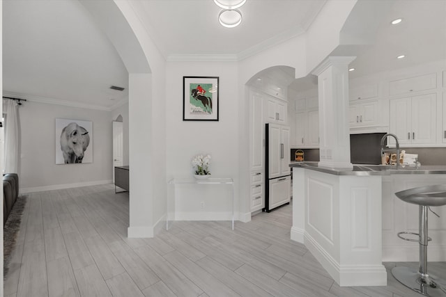 kitchen featuring stainless steel counters, a kitchen breakfast bar, high end refrigerator, kitchen peninsula, and white cabinets