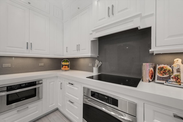 kitchen featuring black electric cooktop, stainless steel oven, white cabinets, and custom range hood