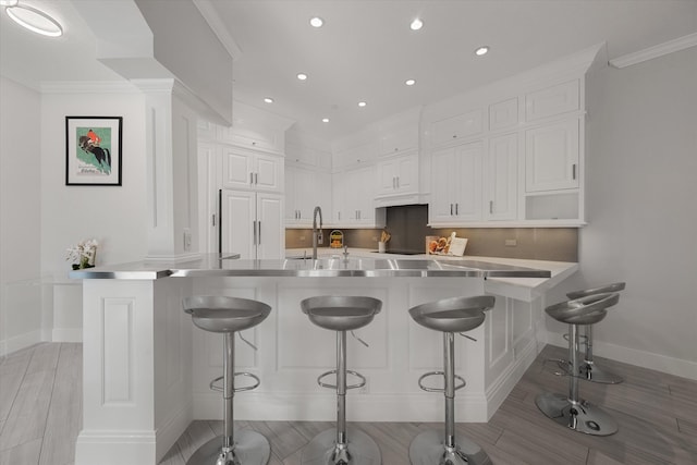 kitchen with white cabinets, a kitchen breakfast bar, ornamental molding, and sink