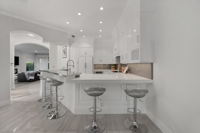 kitchen with backsplash, light hardwood / wood-style flooring, white cabinetry, kitchen peninsula, and a breakfast bar area