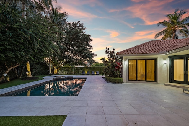 pool at dusk featuring an in ground hot tub and a patio area