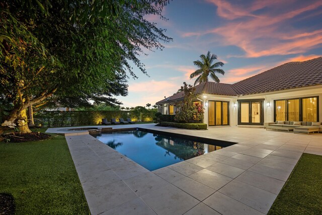 pool at dusk with an in ground hot tub, an outdoor hangout area, a patio area, and a lawn