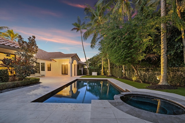 pool at dusk with an in ground hot tub and a patio