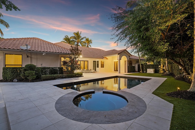 pool at dusk featuring an in ground hot tub, a yard, and a patio