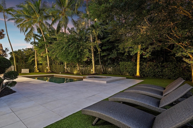 pool at dusk with an in ground hot tub and a patio area