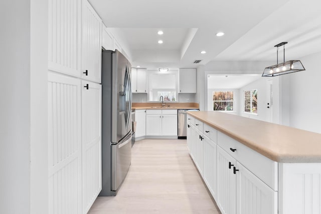 kitchen featuring white cabinetry, a center island, sink, decorative light fixtures, and appliances with stainless steel finishes