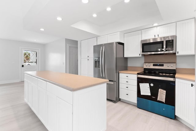 kitchen with light wood-type flooring, stainless steel appliances, a raised ceiling, a center island, and white cabinetry