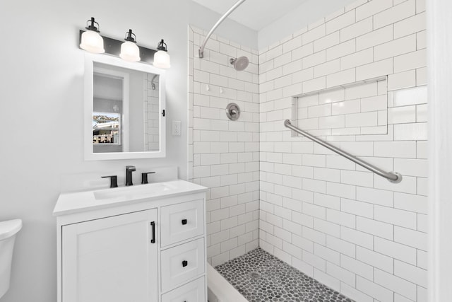 bathroom with a tile shower, vanity, and toilet