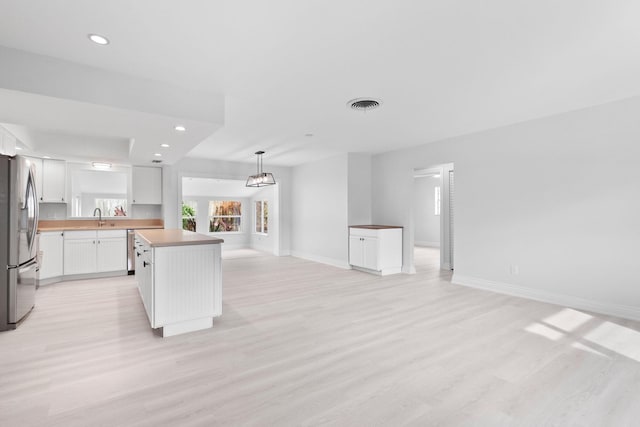 kitchen featuring white cabinets, stainless steel fridge, a kitchen island, and light wood-type flooring