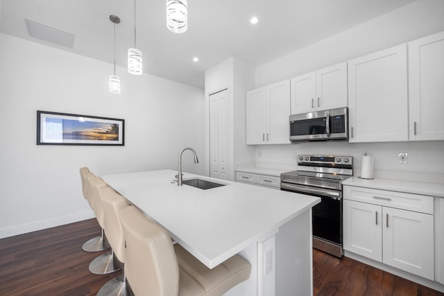 kitchen with pendant lighting, sink, stainless steel appliances, white cabinets, and a center island with sink