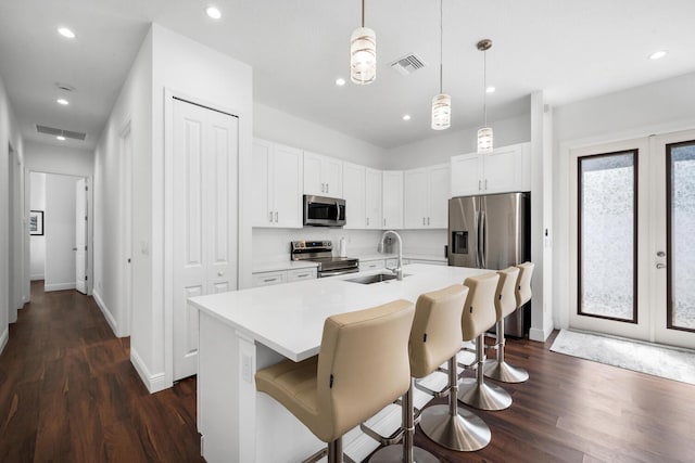 kitchen featuring sink, white cabinetry, decorative light fixtures, stainless steel appliances, and a kitchen island with sink