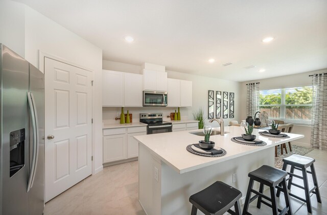 kitchen with light stone counters, stainless steel appliances, sink, white cabinets, and an island with sink