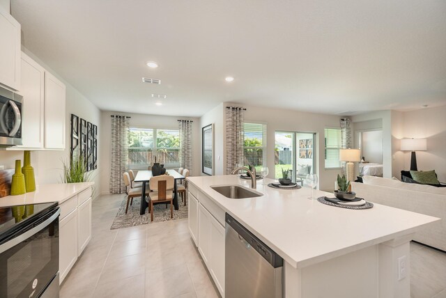 kitchen featuring appliances with stainless steel finishes, light stone counters, sink, a center island with sink, and white cabinets