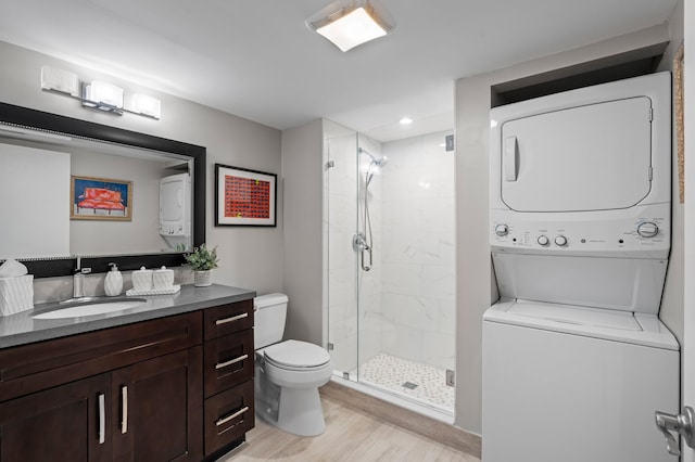 bathroom featuring stacked washer / dryer, hardwood / wood-style flooring, vanity, an enclosed shower, and toilet