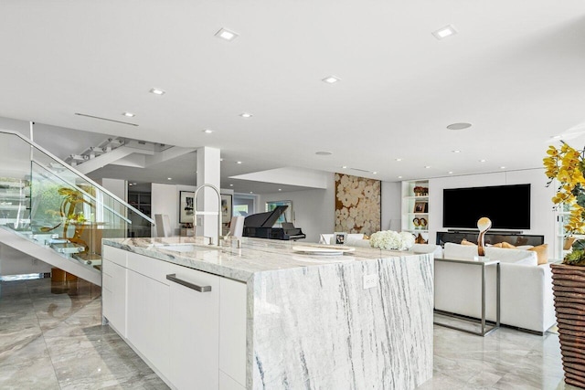 kitchen with white cabinets, a large island with sink, light stone counters, and sink