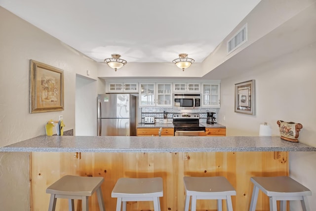 kitchen featuring a breakfast bar area, stainless steel appliances, decorative backsplash, and kitchen peninsula