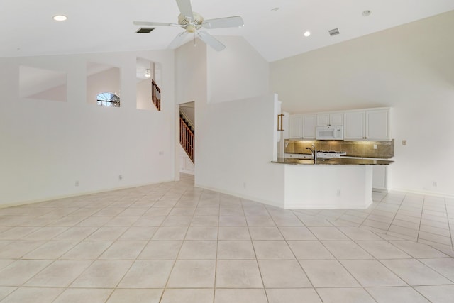 unfurnished living room featuring ceiling fan, sink, light tile patterned floors, and high vaulted ceiling