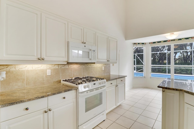 kitchen featuring white cabinetry, white appliances, light tile patterned flooring, and dark stone countertops