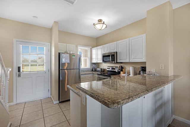 kitchen with kitchen peninsula, light tile patterned floors, white cabinetry, stone counters, and appliances with stainless steel finishes