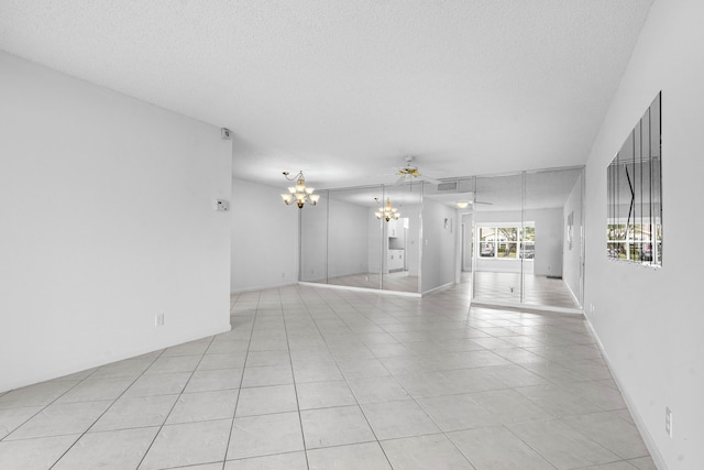 empty room with a textured ceiling, light tile patterned floors, and ceiling fan with notable chandelier