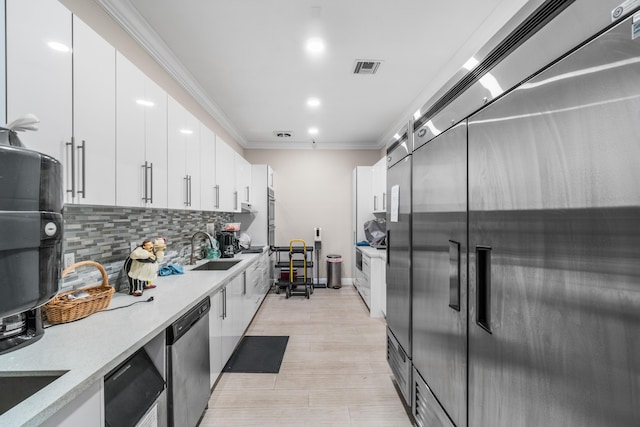 kitchen with appliances with stainless steel finishes, ornamental molding, sink, white cabinets, and light hardwood / wood-style floors