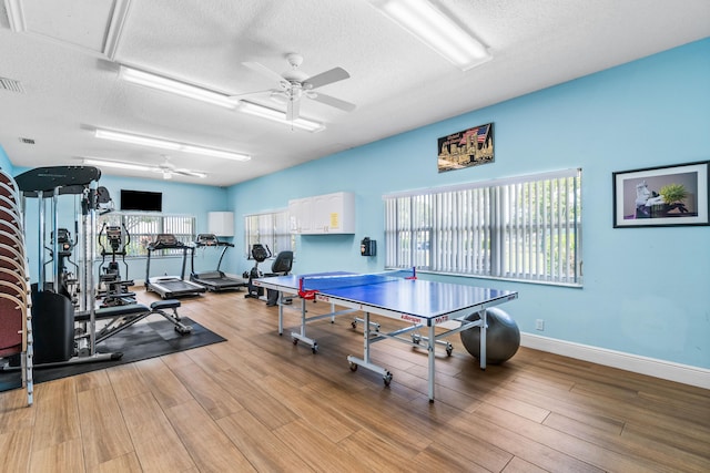 workout area with a textured ceiling, light wood-type flooring, and ceiling fan