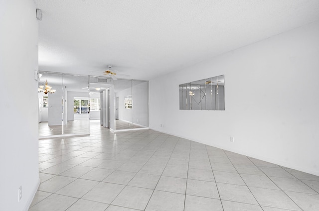 unfurnished room featuring light tile patterned floors, ceiling fan with notable chandelier, and a textured ceiling