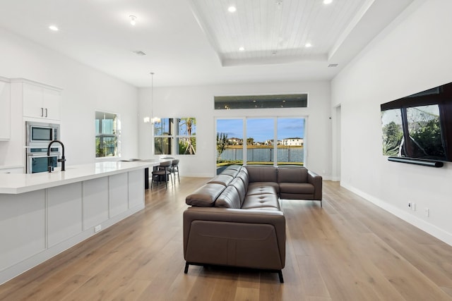 living room with a chandelier, light hardwood / wood-style floors, plenty of natural light, and a tray ceiling