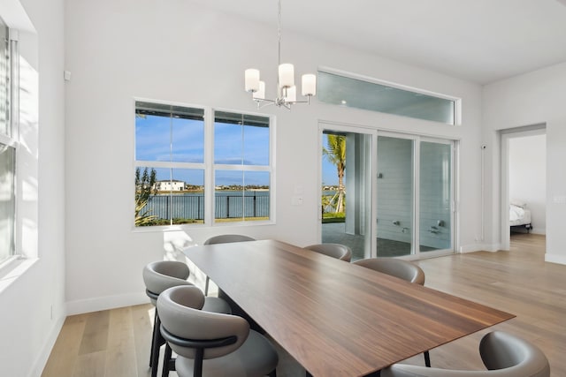 dining area featuring a notable chandelier, light hardwood / wood-style floors, a water view, and a wealth of natural light