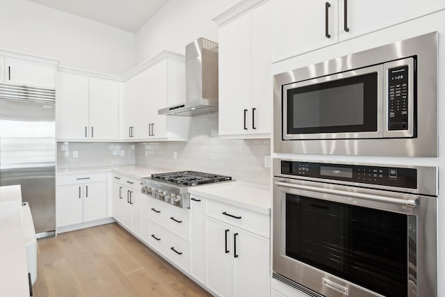 kitchen with decorative backsplash, appliances with stainless steel finishes, white cabinetry, and wall chimney exhaust hood