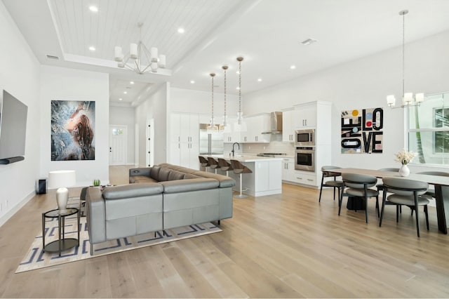 living room featuring a high ceiling, light wood-type flooring, a tray ceiling, a notable chandelier, and wood ceiling