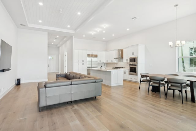 living room featuring wooden ceiling, light hardwood / wood-style flooring, a towering ceiling, a tray ceiling, and a chandelier