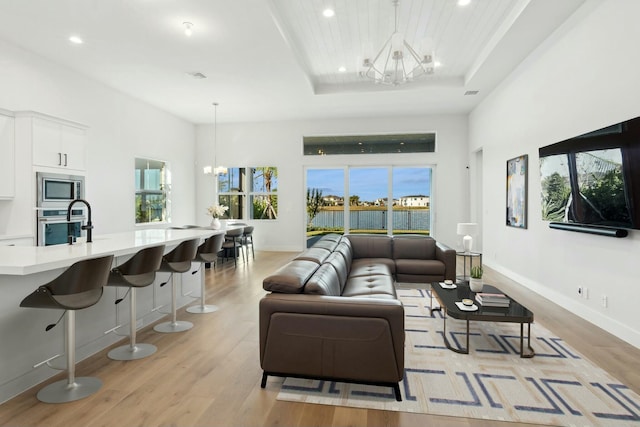 living room with a raised ceiling, light wood-type flooring, and a chandelier