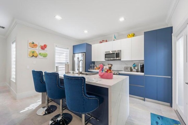 kitchen with a kitchen breakfast bar, stainless steel appliances, crown molding, and a kitchen island with sink