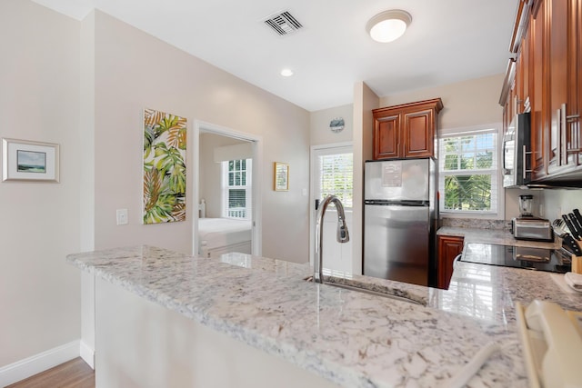 kitchen with kitchen peninsula, appliances with stainless steel finishes, light stone countertops, and sink