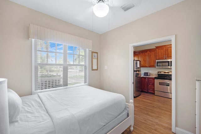 bedroom featuring light hardwood / wood-style floors, ceiling fan, and stainless steel refrigerator