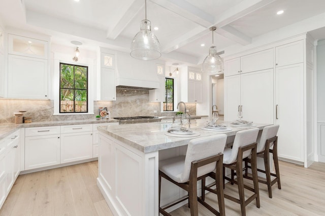 kitchen featuring white cabinets, a center island with sink, light hardwood / wood-style flooring, and custom exhaust hood