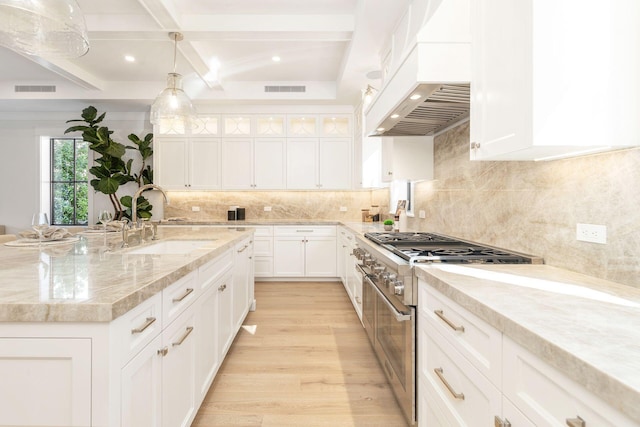 kitchen featuring white cabinets, sink, high end stainless steel range oven, decorative light fixtures, and custom range hood