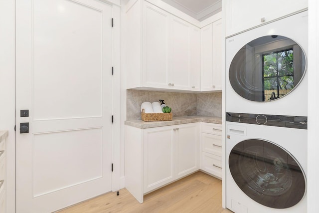 laundry room with light hardwood / wood-style flooring, cabinets, and stacked washer / drying machine