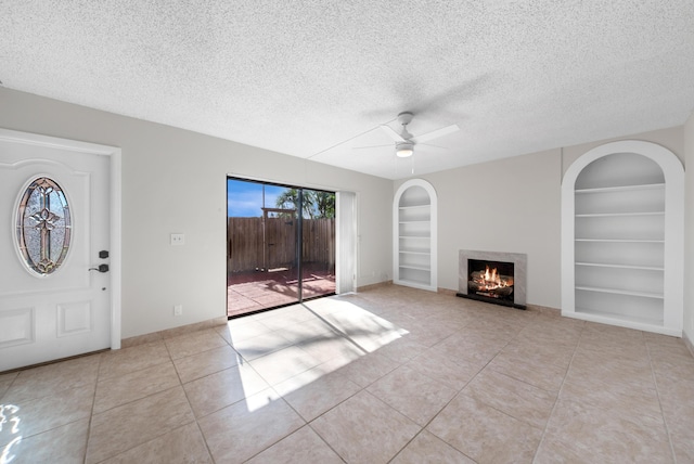 unfurnished living room featuring built in shelves, a textured ceiling, ceiling fan, and light tile patterned flooring